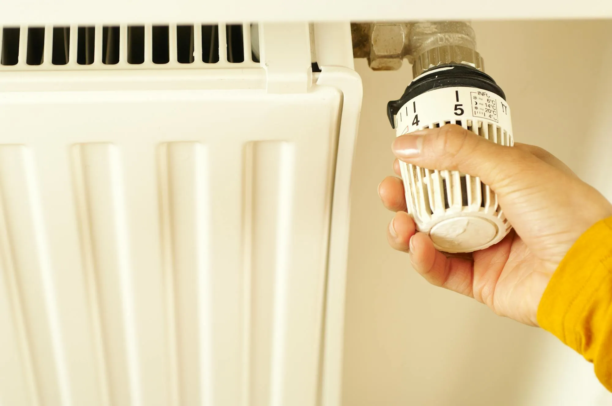 Hand adjusting a thermostatic radiator valve on a UK panel radiator